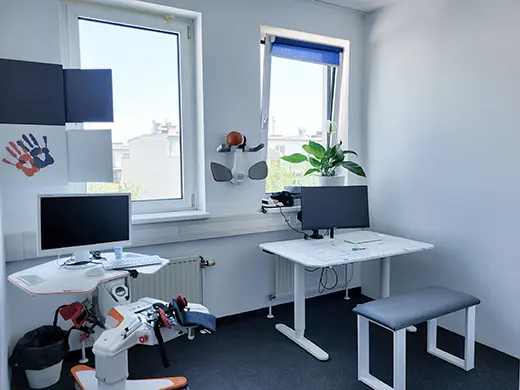 Arbeitsplatz mit zwei Bildschirmen und einem Therapiegerät für Arm und Hand