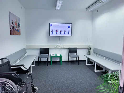 Besprechungsraum mit Bildschirm, Sitzbank und einem Rollstuhl