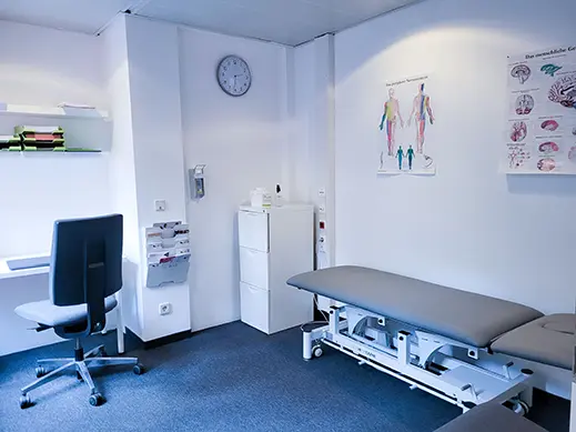 Behandlungsraum mit Therapieliege, Wanduhr und Anatomietafeln