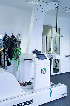Robotikgestütztes Gangtherapiegerät, daneben Gurte und ein Spiegel