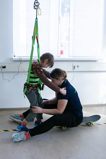 Kind übt Gehen in einem Gurt an der Deckenschiene im Gangtrainingsraum in Graz