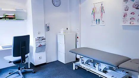 Behandlungsraum mit Therapieliege, Bürostuhl und Anatomietafeln