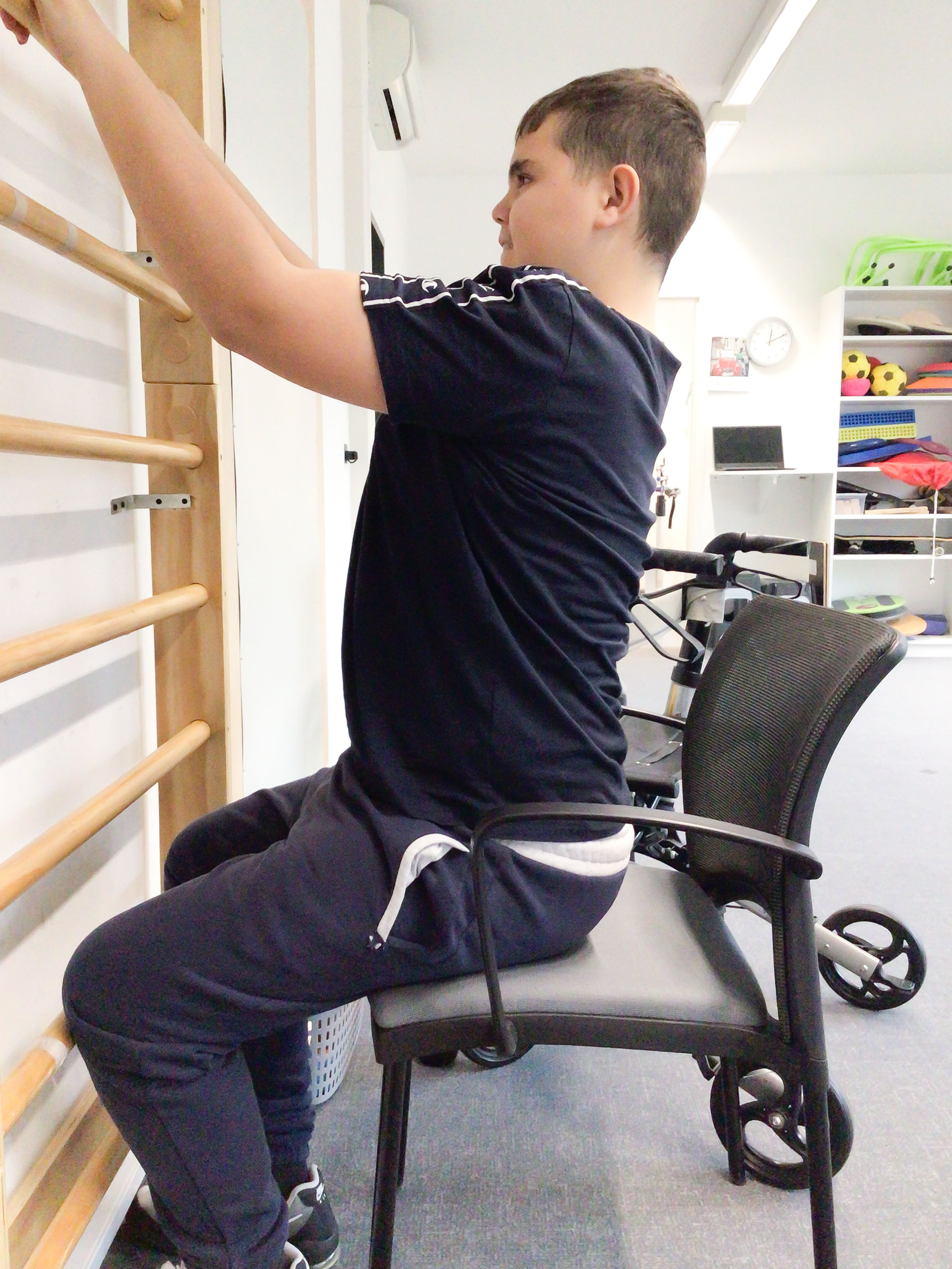 Alina übt mit Holzblöcken auf einer Therapiemappe am Boden. Therapeutin im Schneidersitz vor ihr