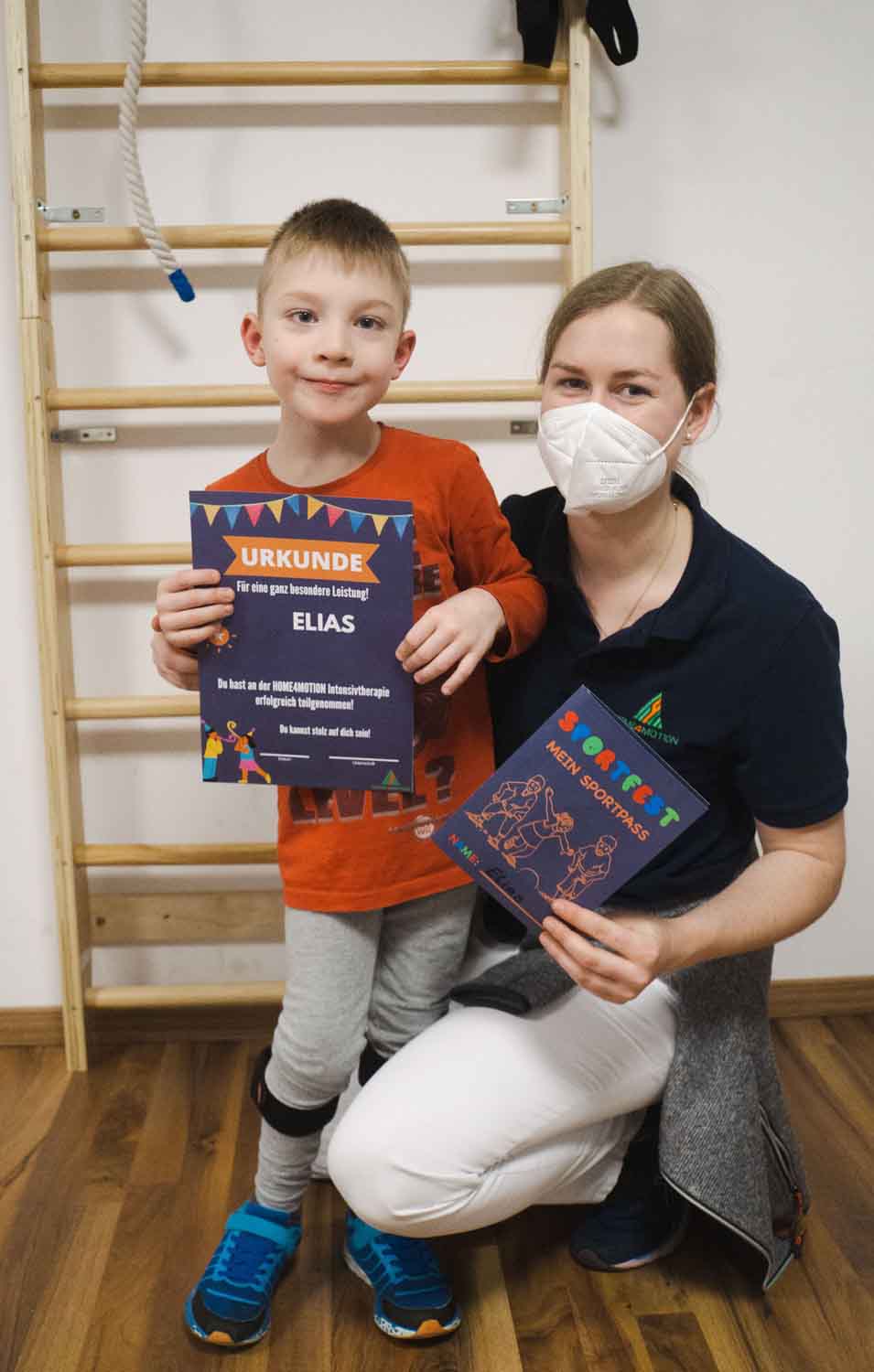 Kind mit der Therapeutin und Urkunde am Sprossenwand