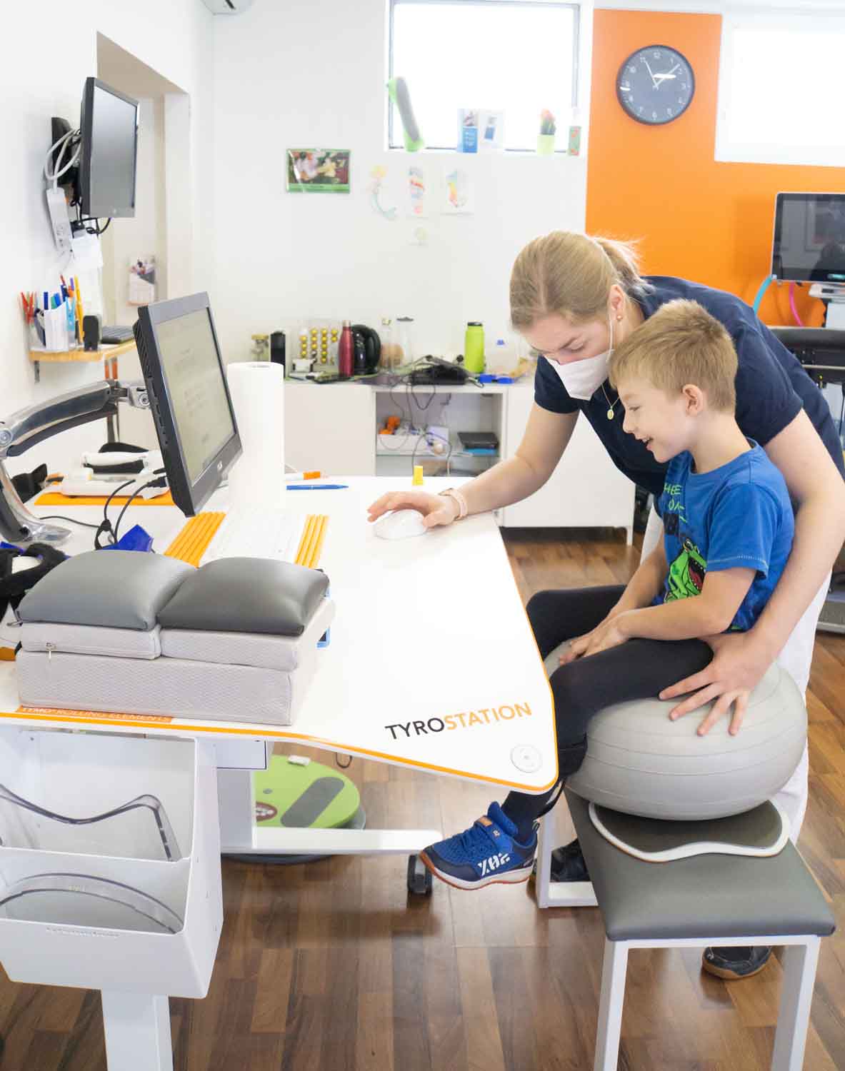 Ein Kind am Pablo macht Übungen am Ball mit Therapeutin