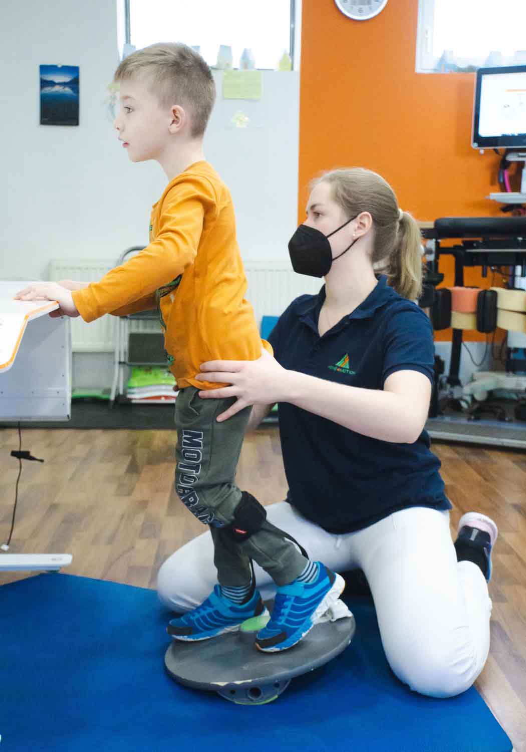 Ein Kind am Tymo macht Übungen mit Therapeutin