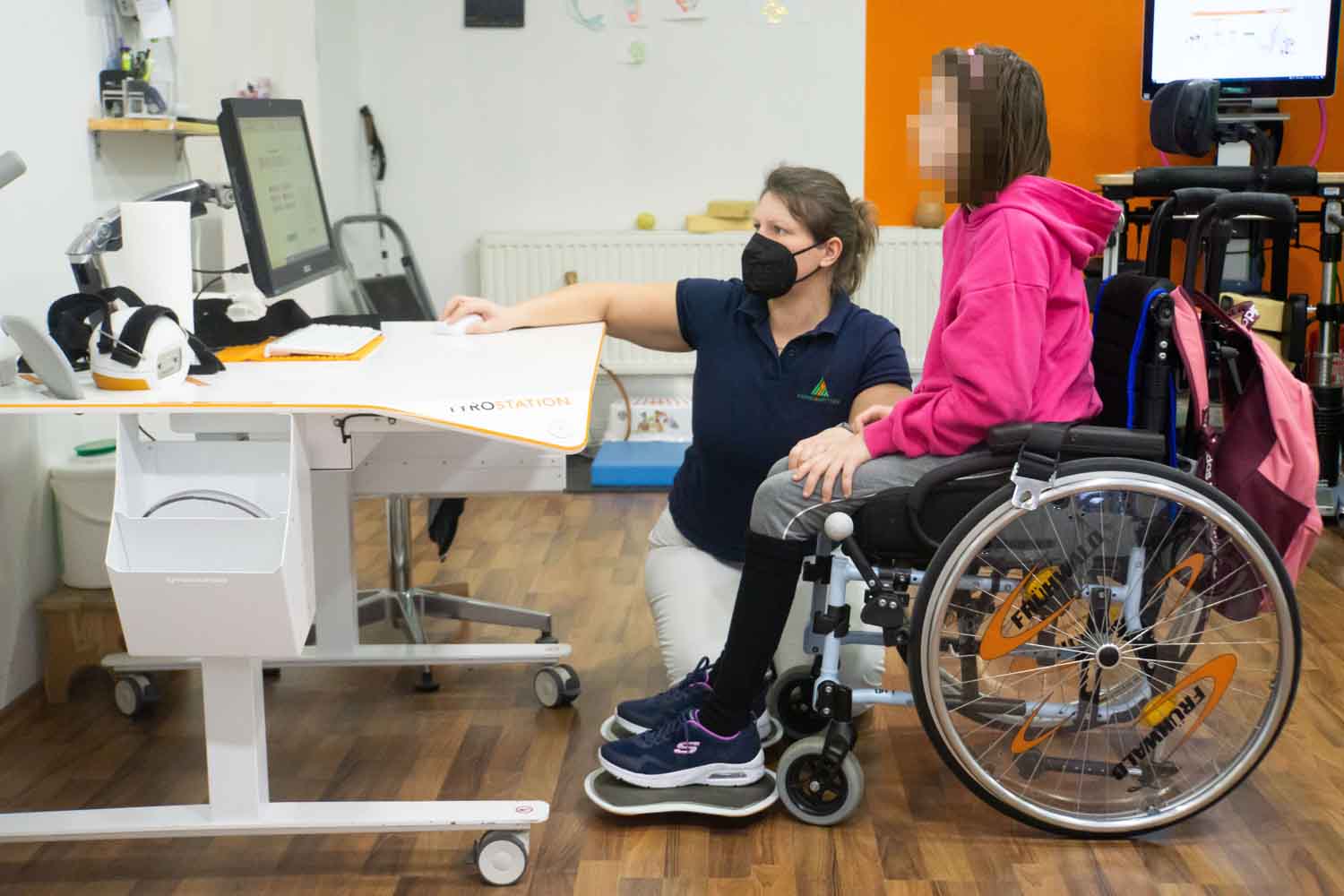 ein Kind im Rollstuhl macht Übungen mit Therapeutin