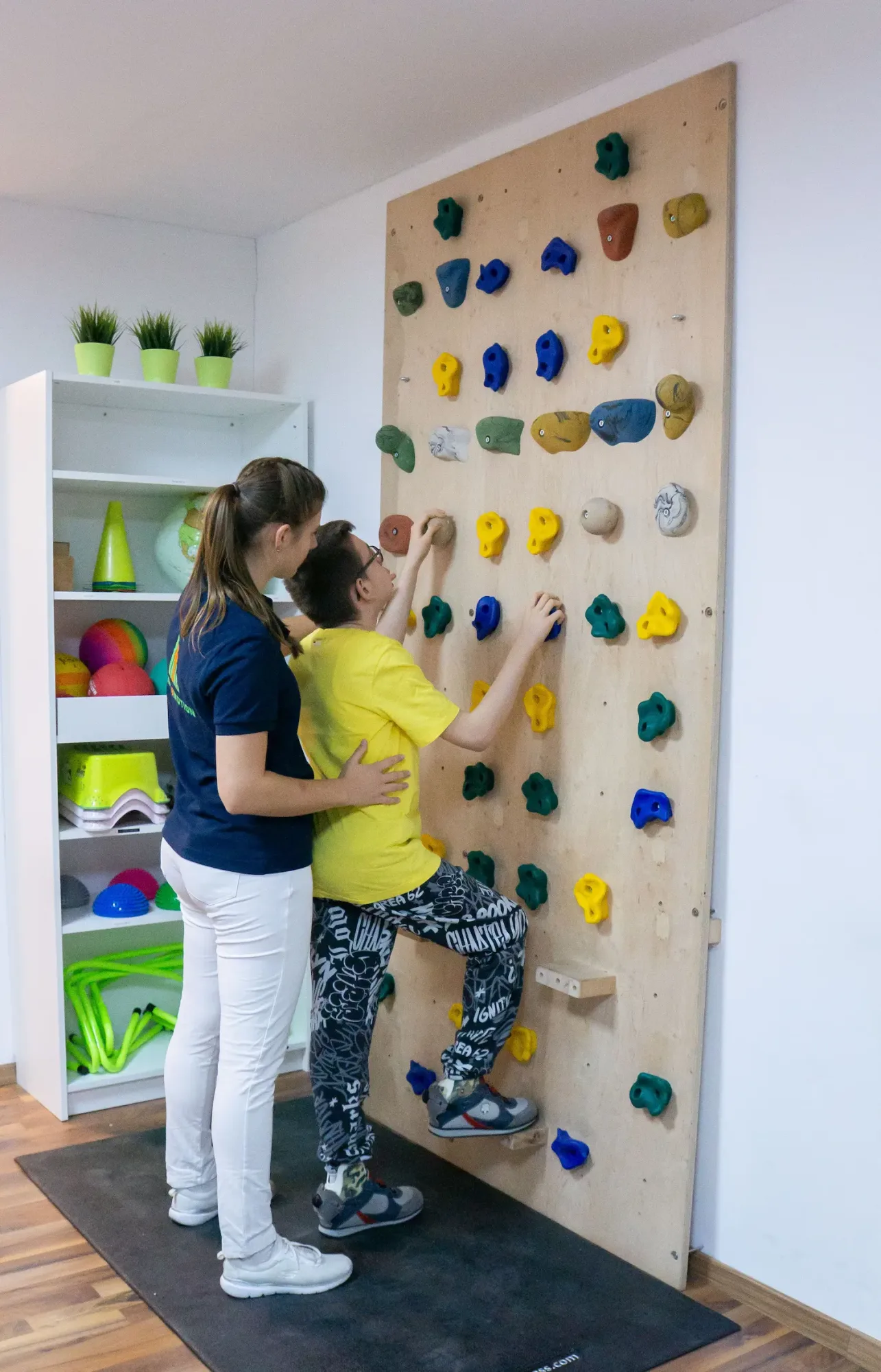 Kind am Kletterwand und Therapeutin unterstützt