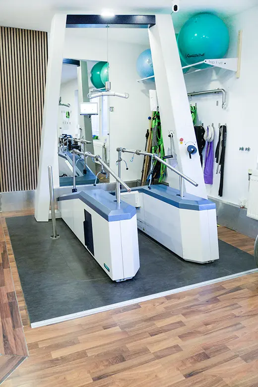 Gangtrainer mit Aufhängung, daneben Therapiematerial und Gymnastikbälle an der Wand