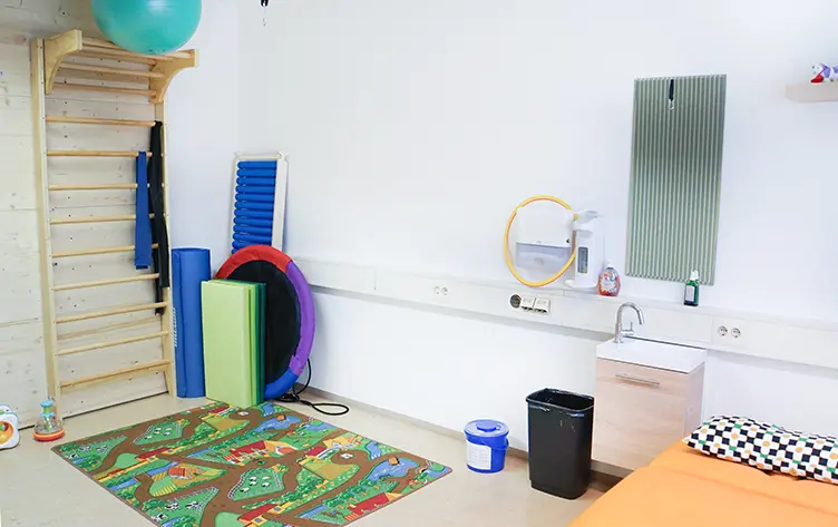 Kindertherapieraum mit Sprossenwand, Schaumstoffrollen, Balancereifen und Spielteppich