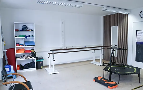 Gehbarren und Trampolin neben einem Regal mit Therapierollen und Bällen