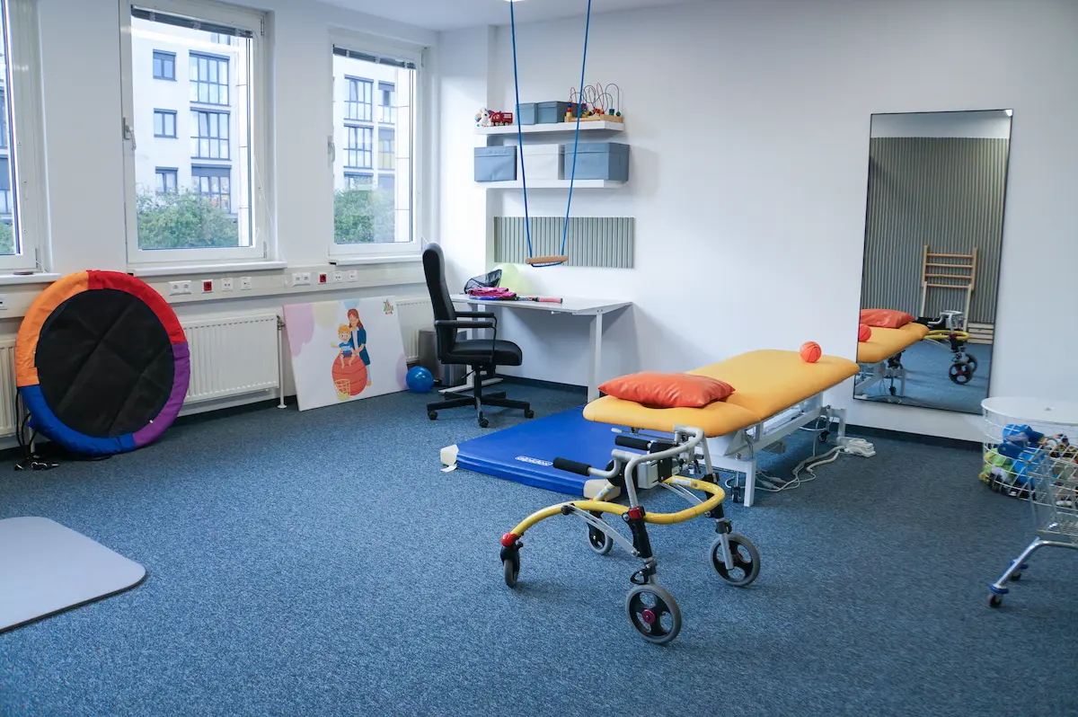 Bunte Therapieliege mit Gurten, daneben Balancereifen und ein großer Spiegel