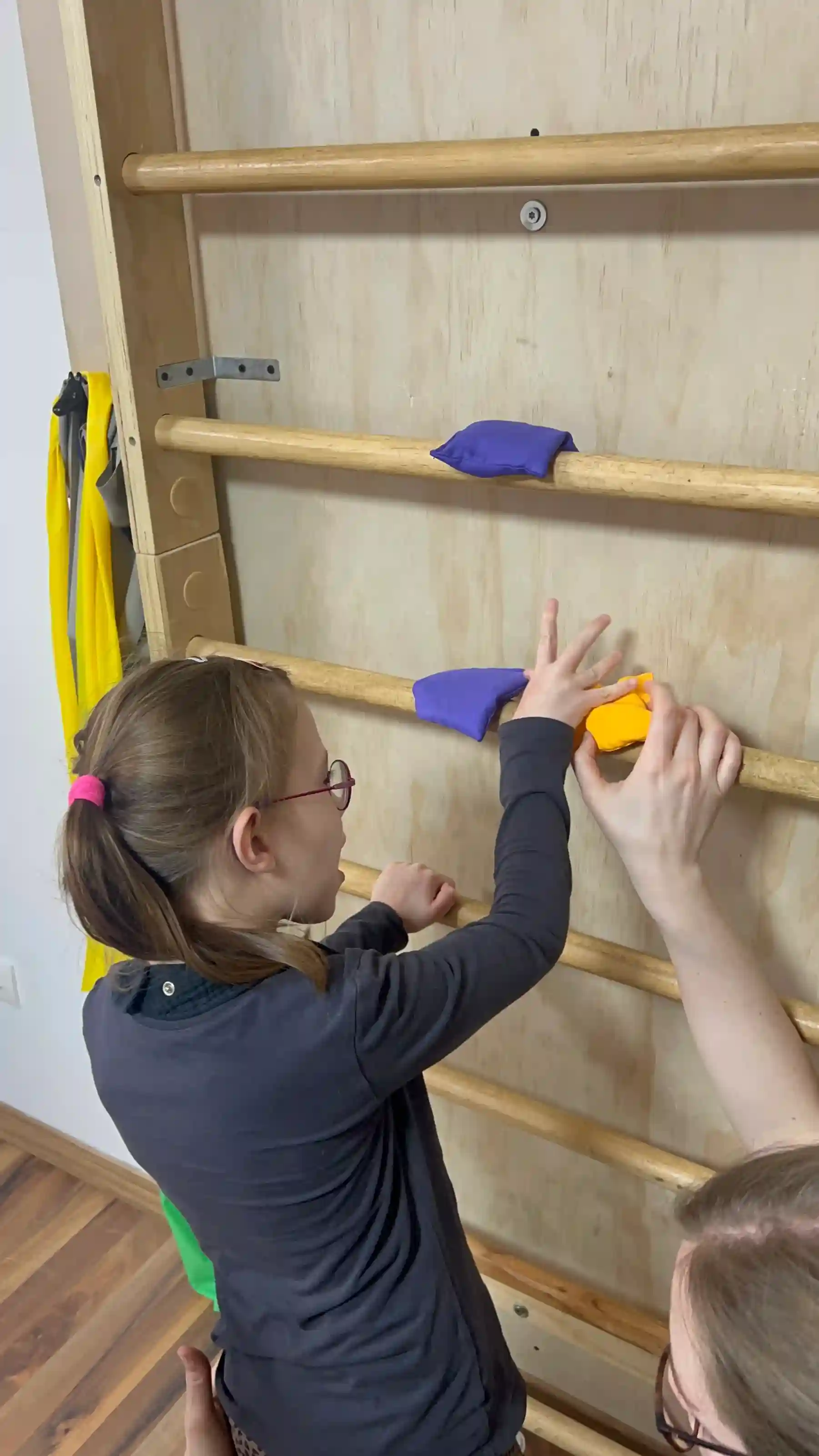 A child places colourful climbing holds on a wooden wall