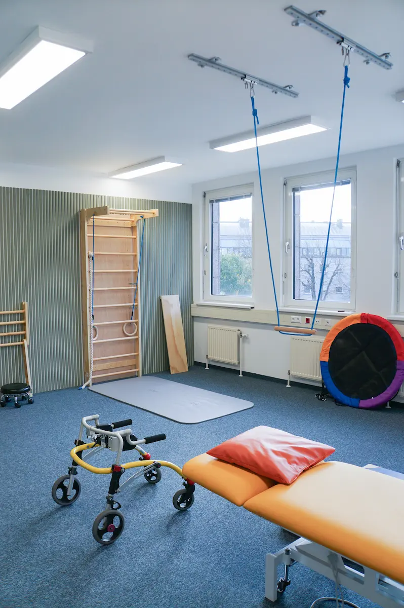 Sprossenwand aus Holz mit Deckenaufhängung, davor eine Therapieliege